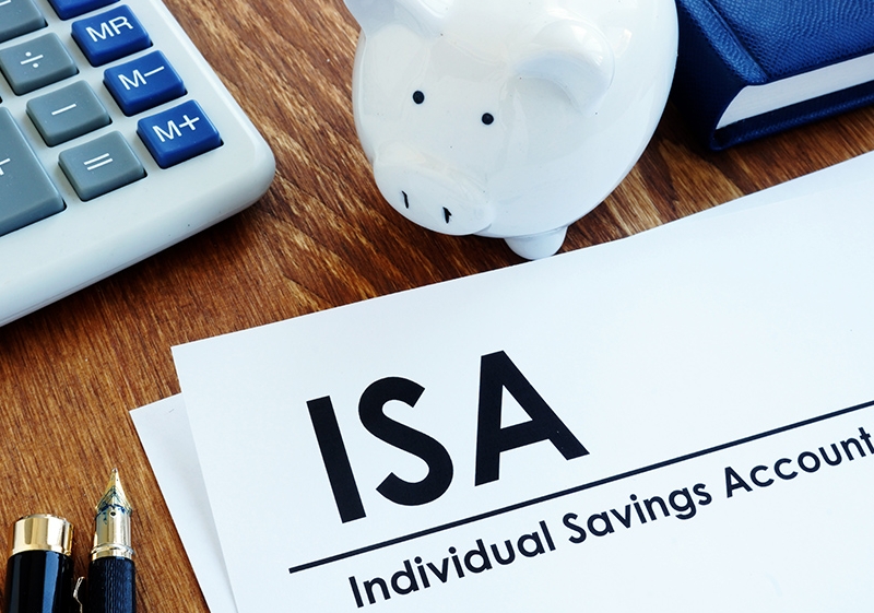 계산기, 볼펜, 돼지저금통, 책, 종이가 보이는 사진 이미지. 종이 위에는 검정 글씨로 ISA, Individual Savings Account라고 적혀있다.