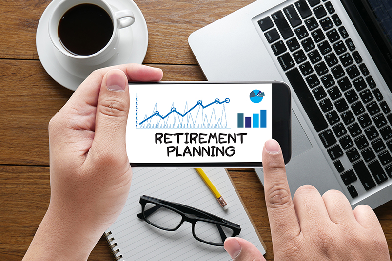 노트북, 커피, 노트, 스마트폰 화면이 나타난 사진. 스마트폰 화면에는 영문으로 RETIREMENT PLANNING 이라고 적혀있다.