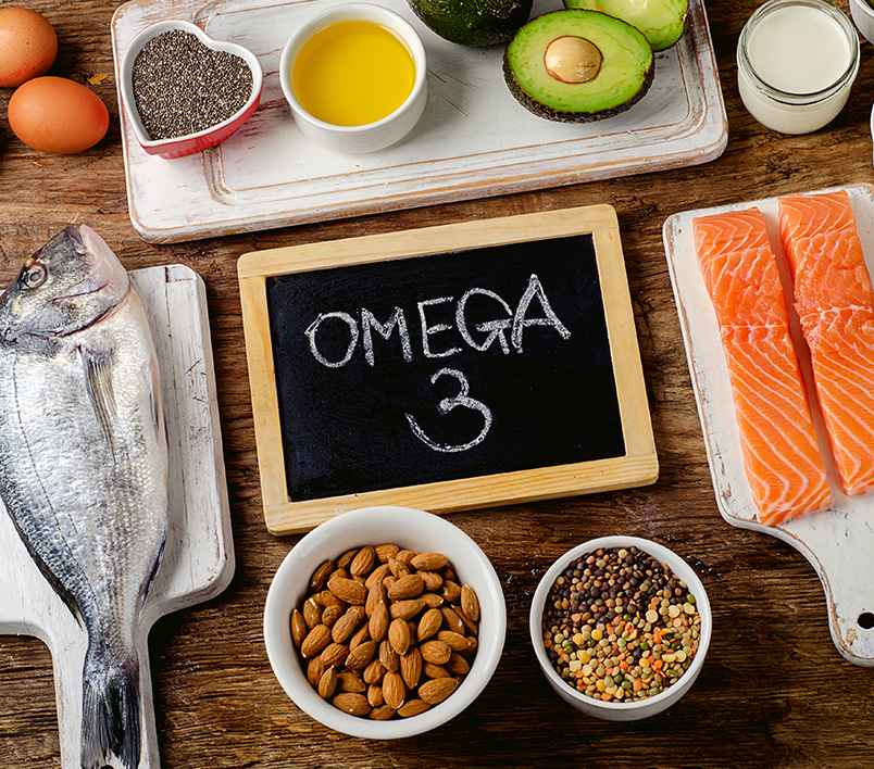 원목 테이블위에 'OMEGA3'라고 적힌 미니 칠판과 생선, 계란, 아몬드, 아보카도, 연어 등이 있다.