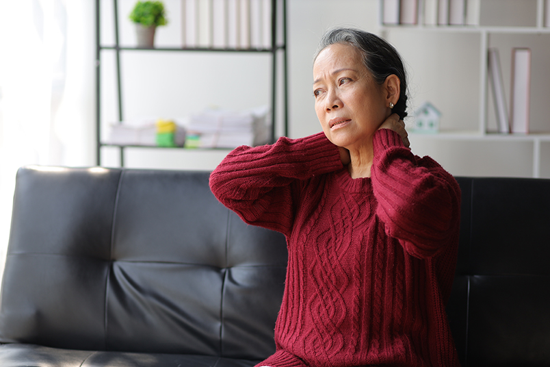 검정색 '가죽 소파' 위에 앉아 있는 '백발 할머니' . 빨간색 니트를 입고, 양손 모두 목을 움켜쥔 채 '인상' 을 쓰고있음.