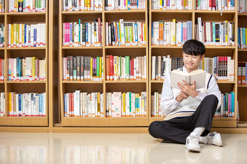 어린 남학생이 '도서관'에서 바닥에 앉아 '책'을 읽고 있는 모습이다.