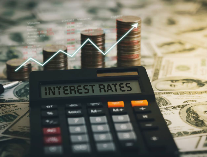 'INTEREST RATES'가 써져있는 계산기 뒤로 동전이 쌓여있다. 동전 4열로 쌓여있으며 우측으로 갈수록 점점 높아지는 형태로, 동전과 함께 우상향하는 화살표가 그려져있다.