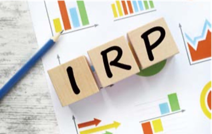 여러 그래프가 있는 서류를 배경으로 'IRP'가 적힌 나무 큐브가 위치해있다.